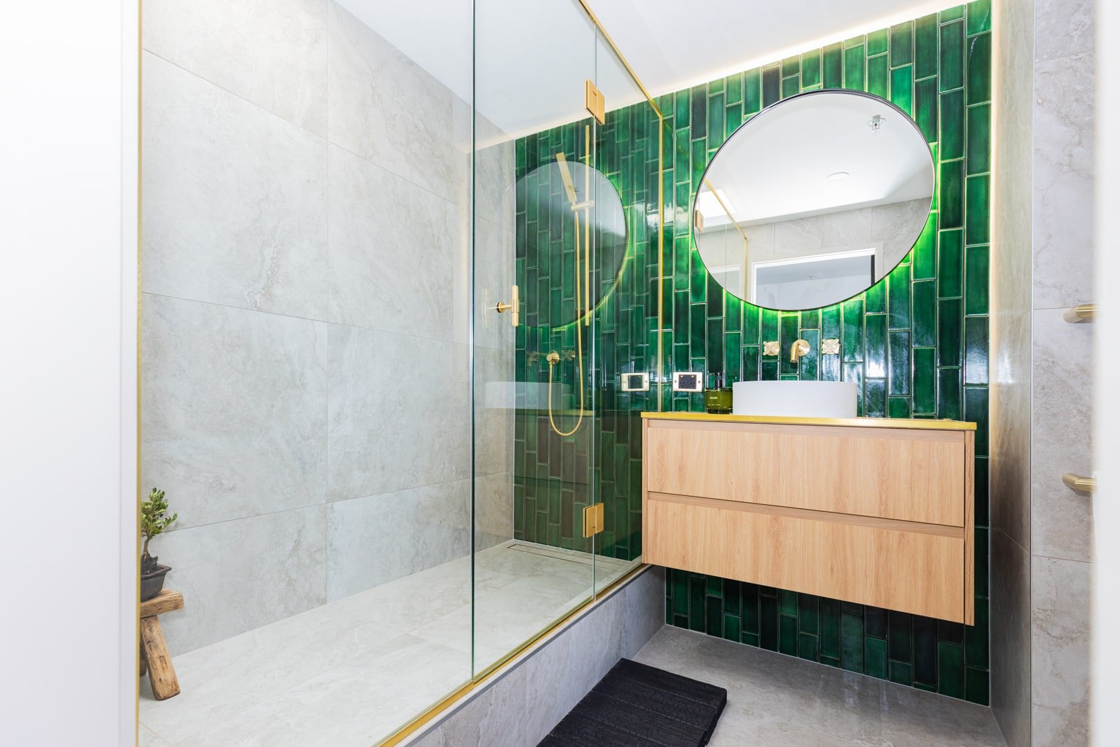 Striking bathroom renovation in Auckland with green feature wall, gold fittings, and floating timber vanity by Sync Renovations.