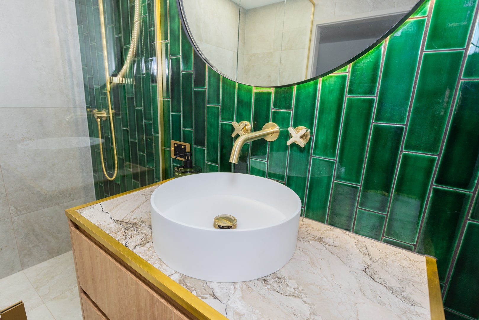 Luxurious bathroom vanity with green subway tiles, brass tapware, and marble countertop by Sync Renovations in Auckland.