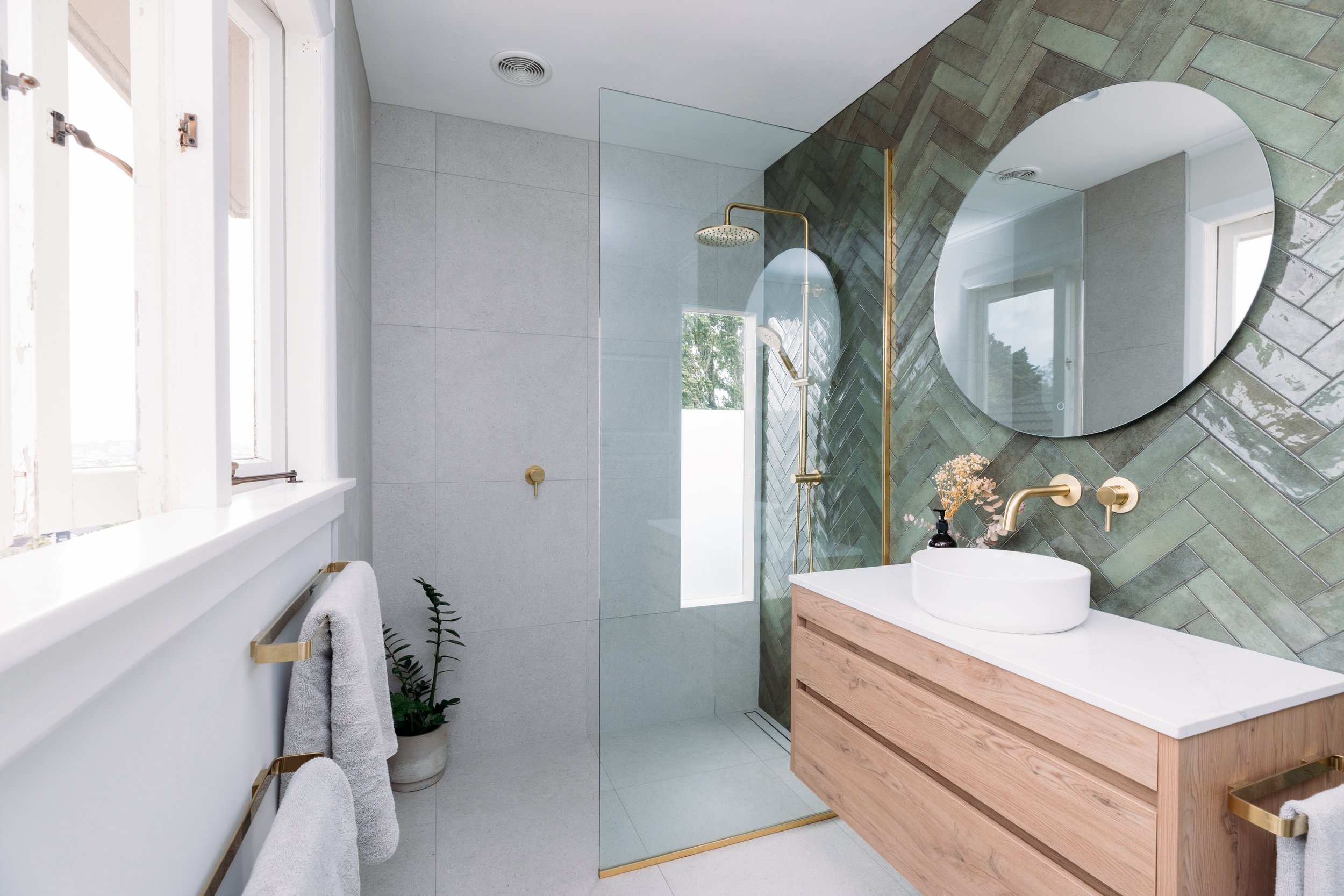 Modern ensuite renovation in Auckland featuring green feature tiles, round mirror, and timber vanity by Sync Renovations.