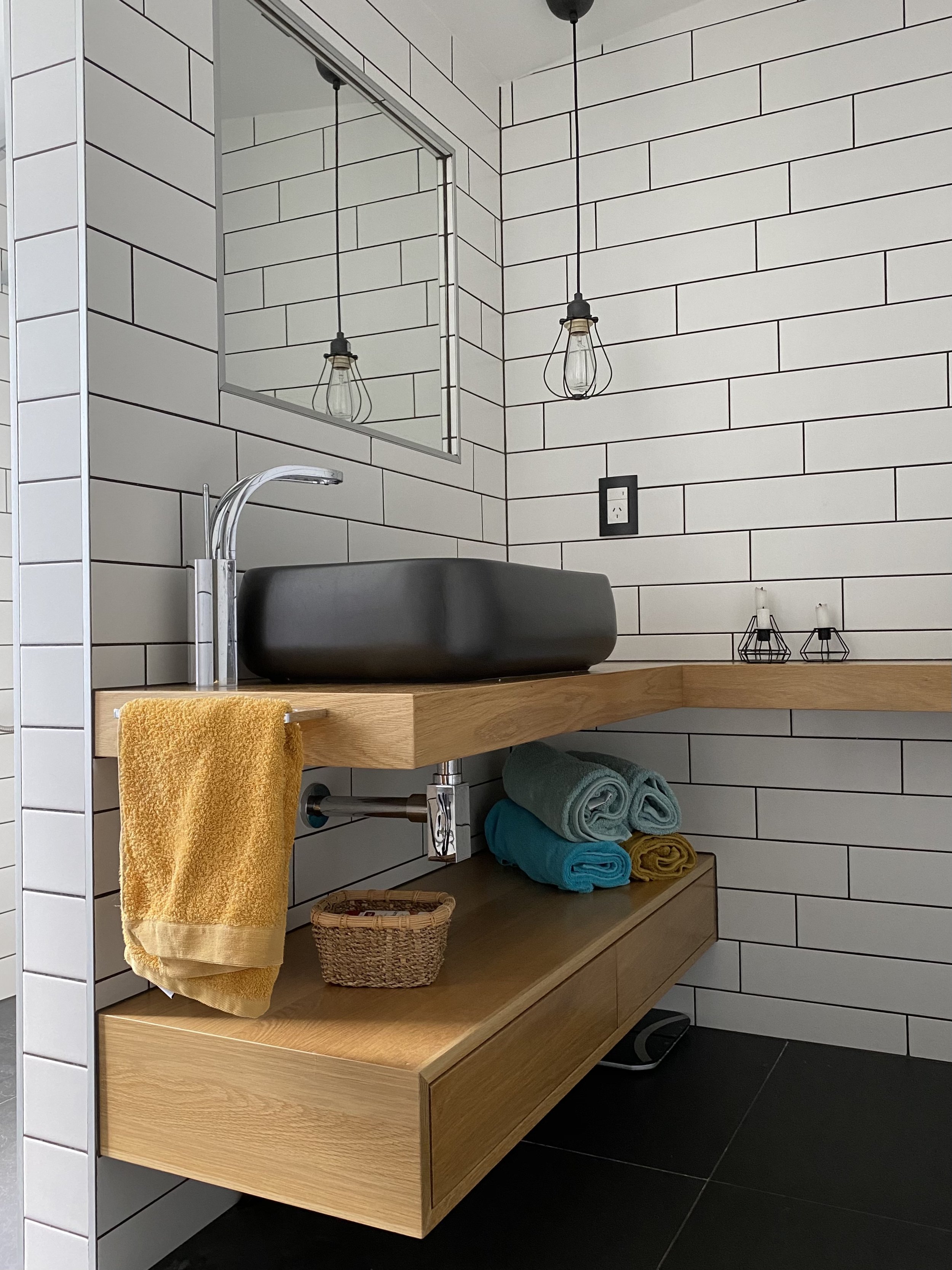 Compact bathroom renovation with black basin, open timber shelving, and subway tiles by Sync Renovations in Auckland.