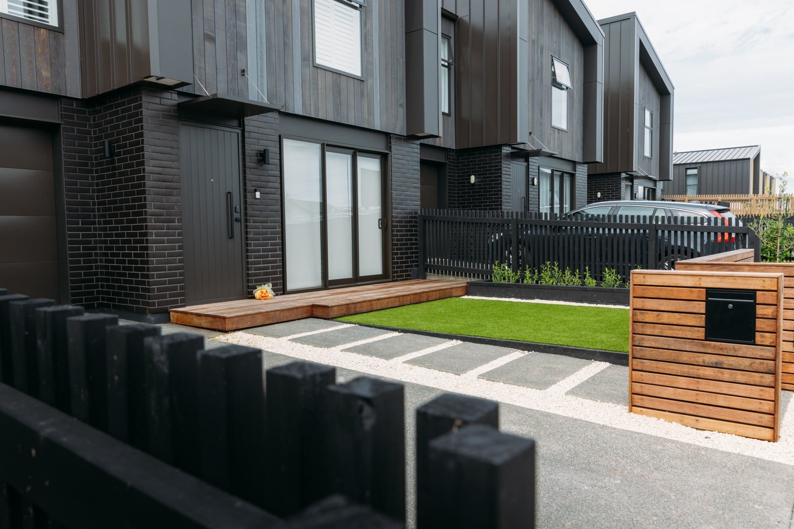 Contemporary outdoor renovation in Auckland with raised timber deck, lawn, and fencing by Sync Renovations.