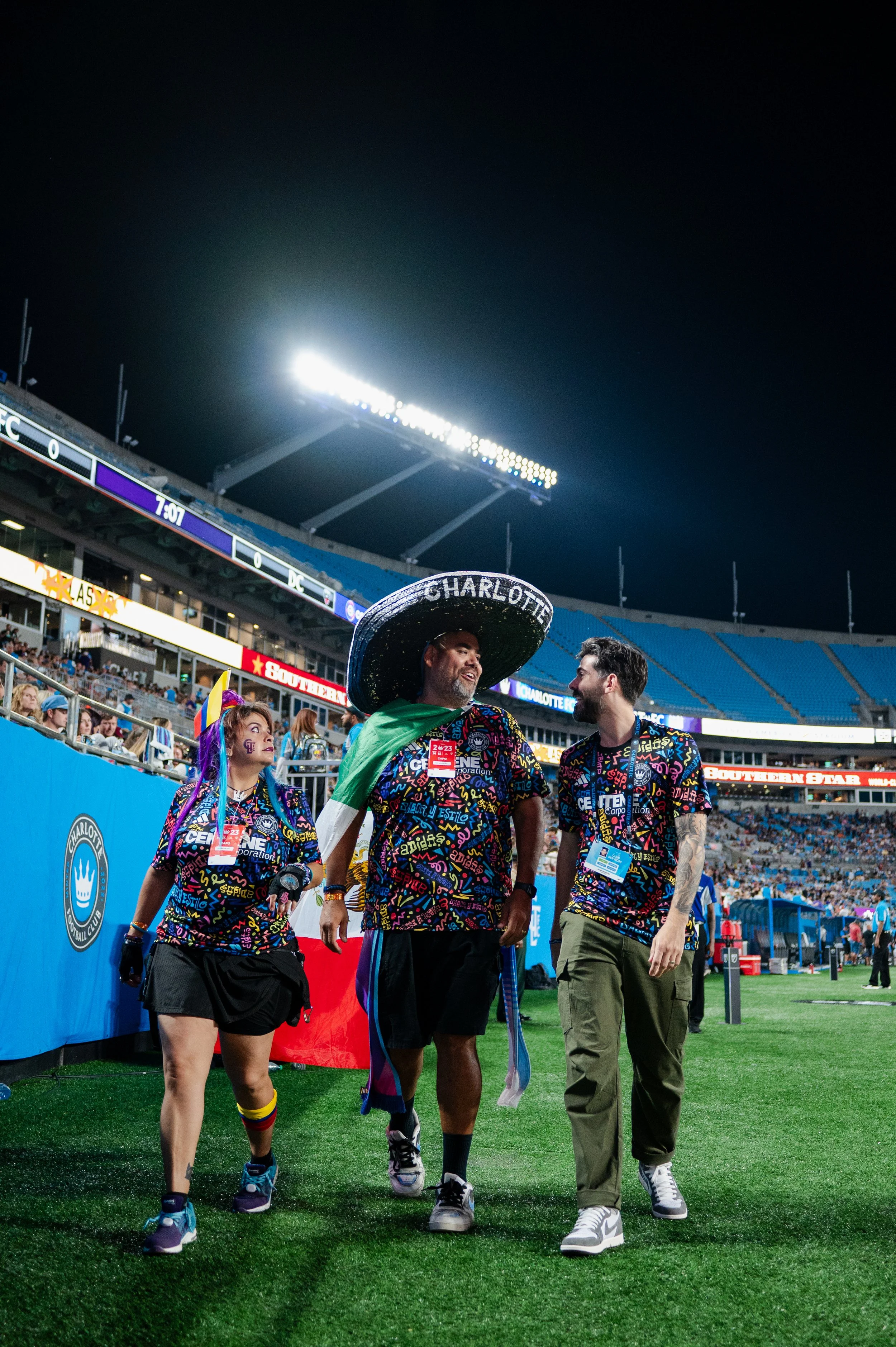  Hector smiling as he walks and chats on the field with two other Charlotte supporters.