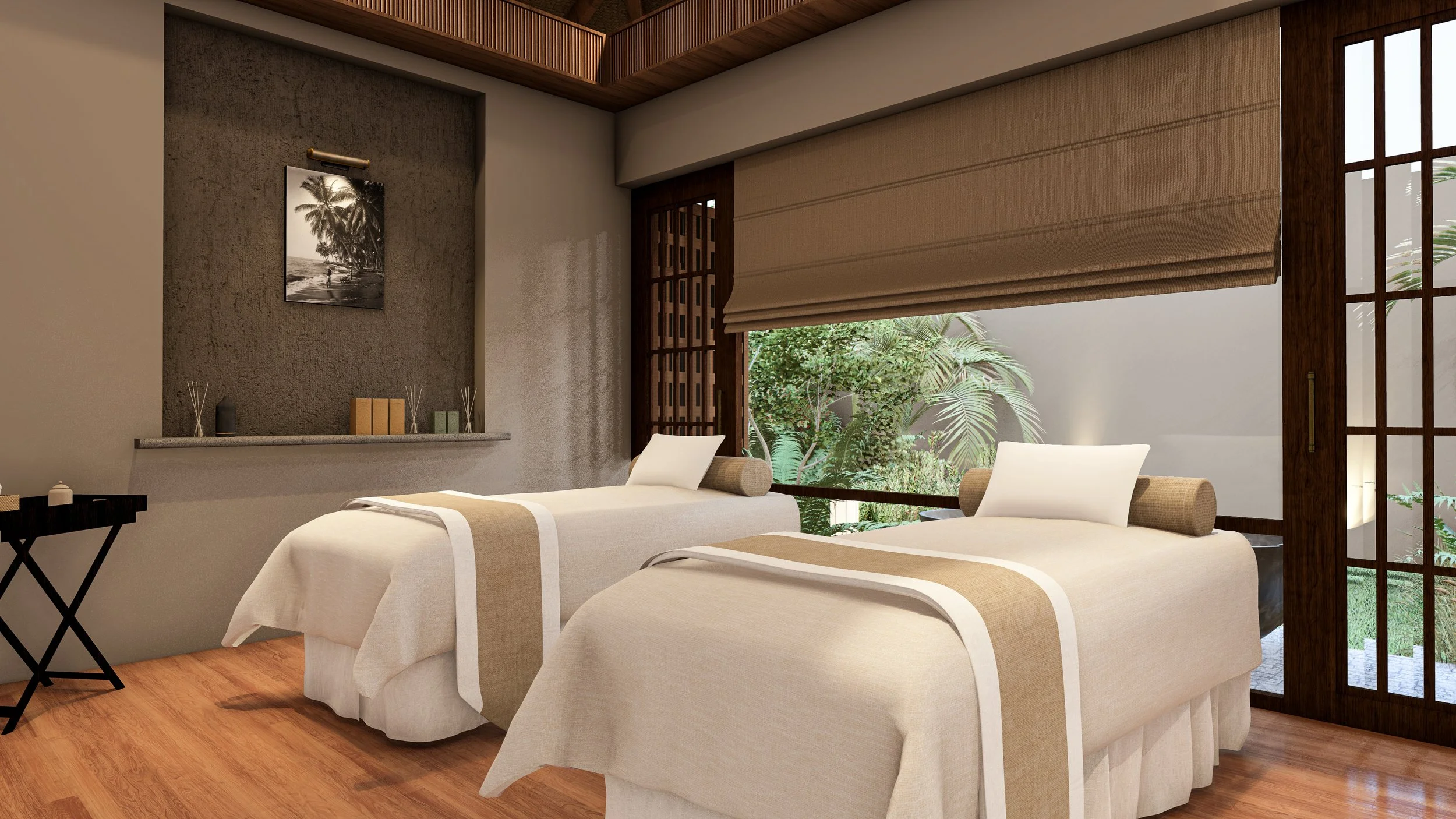 A wellness or spa room with two massage beds draped in white linens with beige accents, positioned side by side near large windows showing greenery outside. The room has wooden accents, a textured wall with a black and white photograph of palm trees,