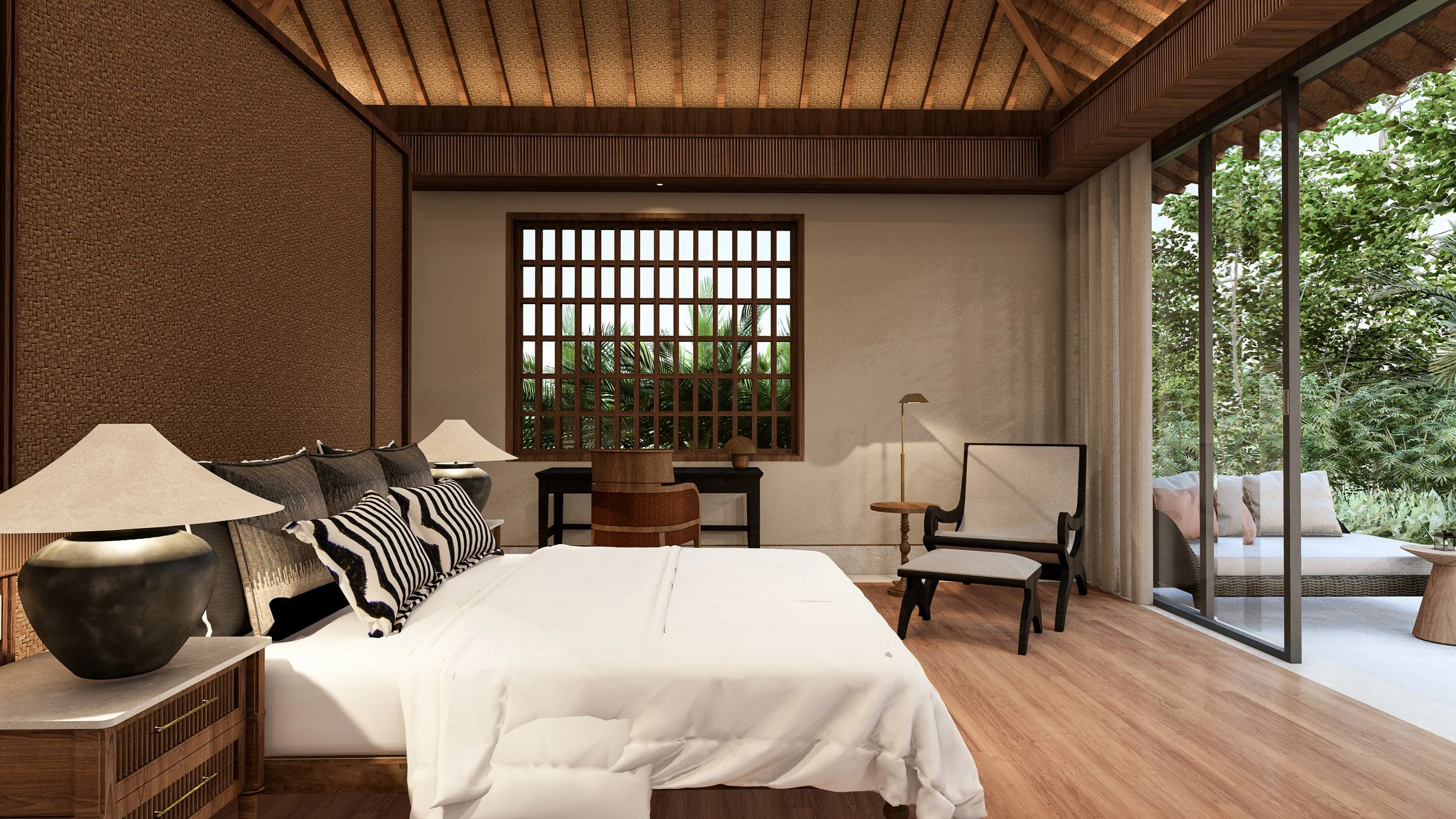 Interior of a bedroom with a white bed, black and white striped pillows, two black and beige lamps on bedside tables, wooden flooring, a sitting area with two chairs, a wooden desk with a chair, and large windows showing lush greenery outside.