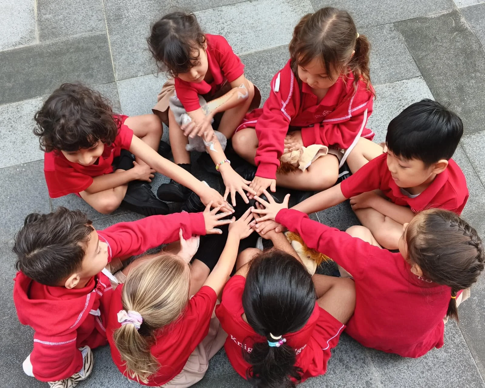 A group of Knightsbridge House expatriate students sitting in a circle  playing outdoor activity with their hands stretchedout
