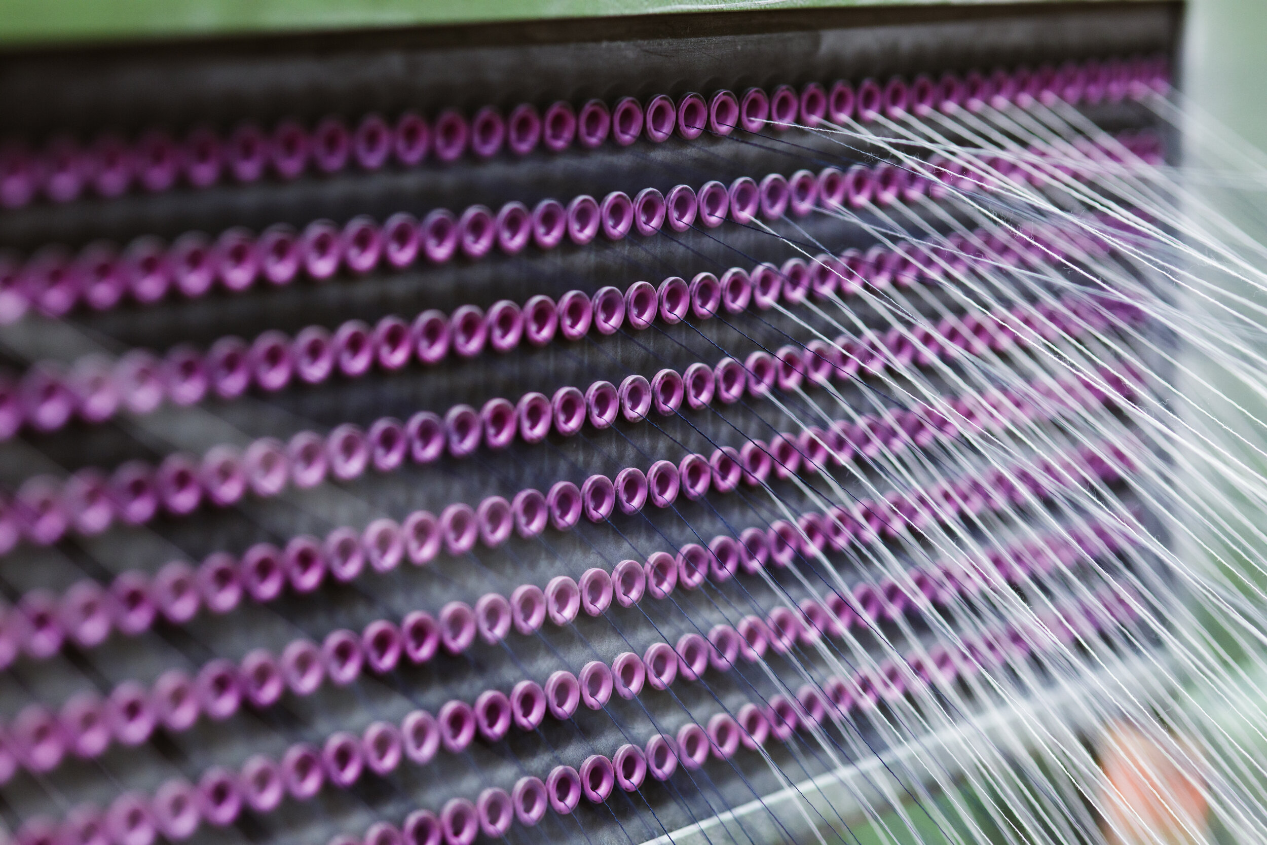 Close-up of a knitting machine with purple yarn loops on metal needles.