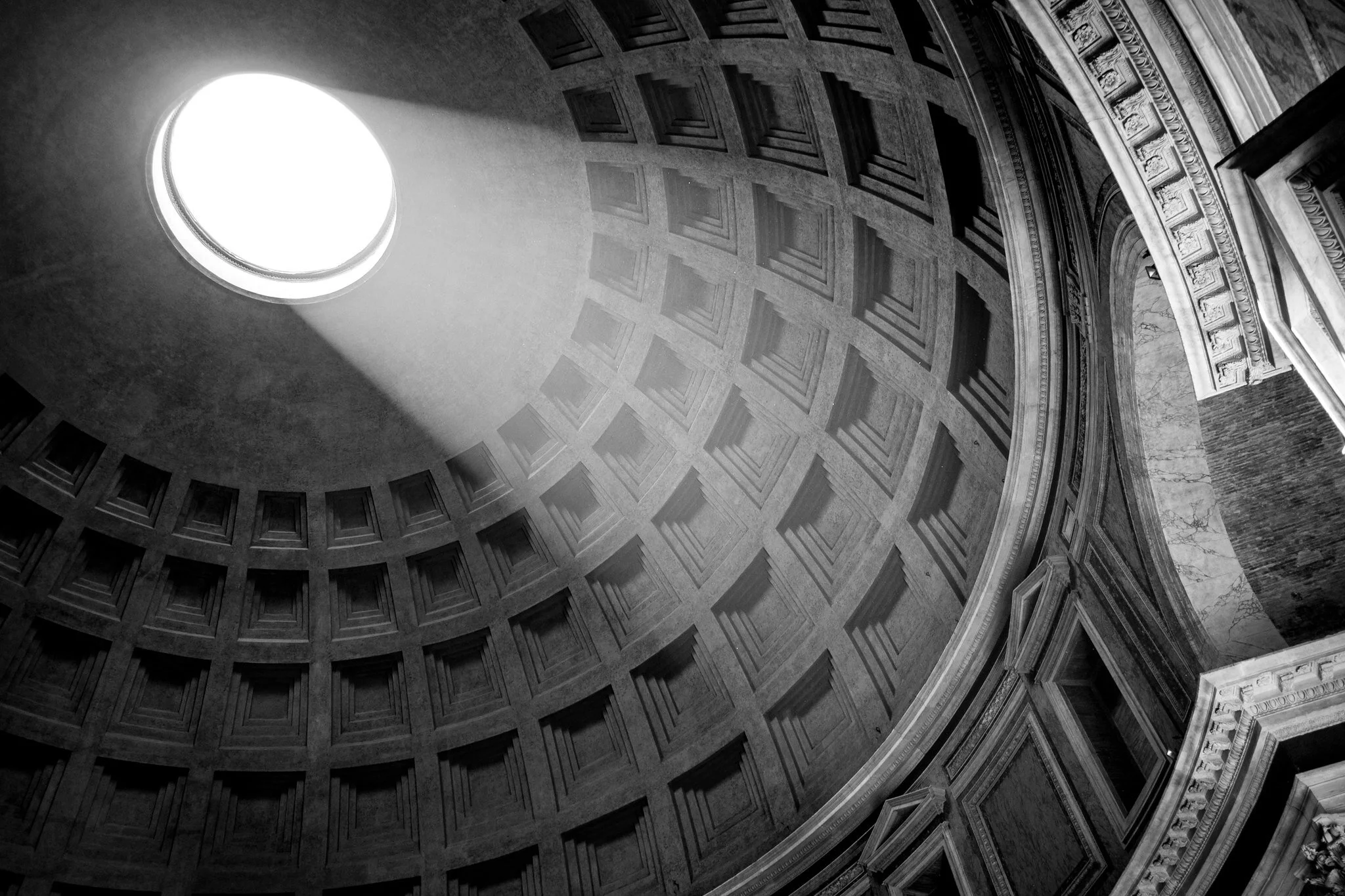 Interior view of the Pantheon in Rome, with the sky visible above and the surrounding architectural features of the colonnade and arches.