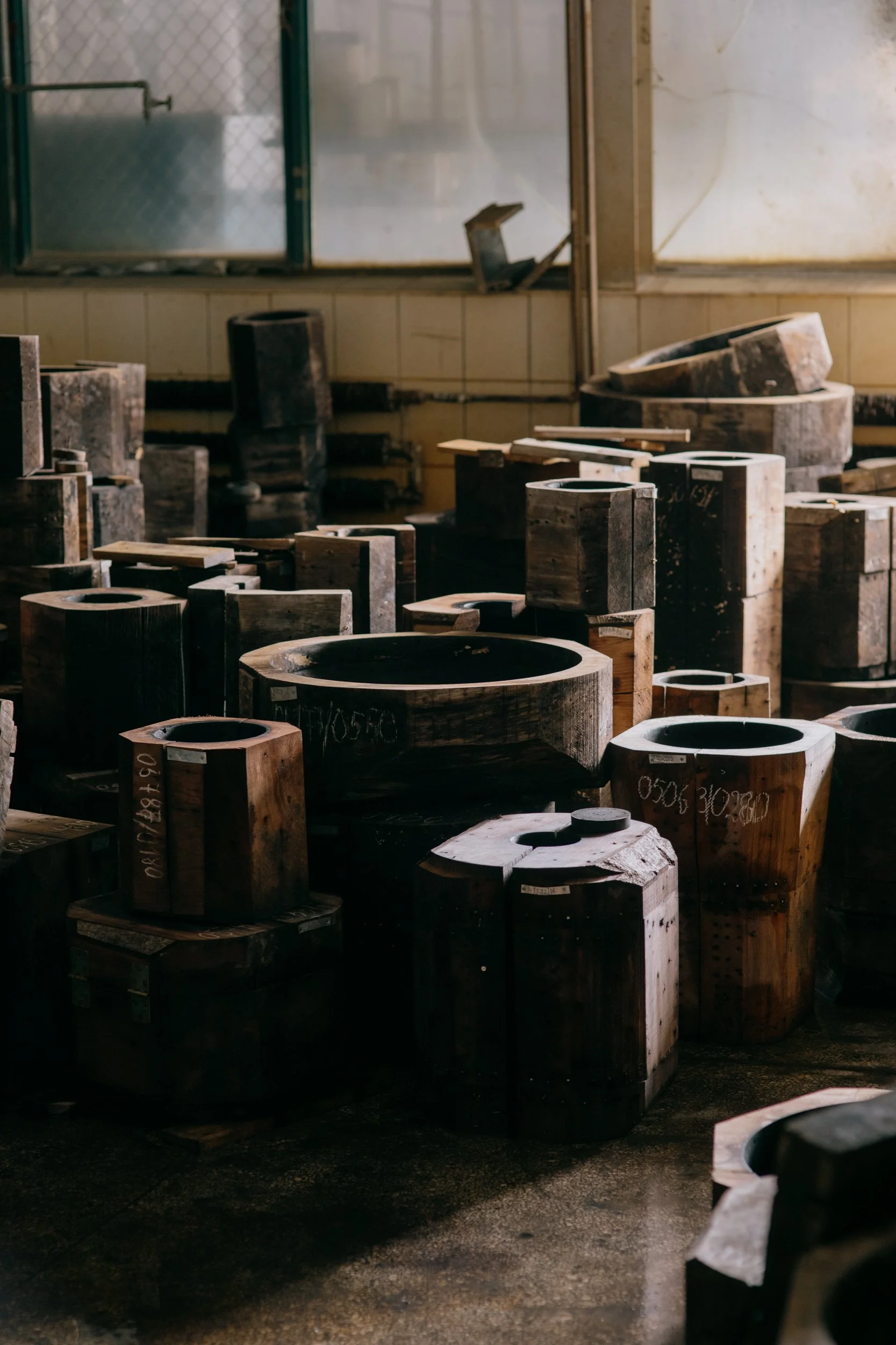 An industrial workshop with large wooden molds and equipment, dimly lit with sunlight filtering through dirty windows.