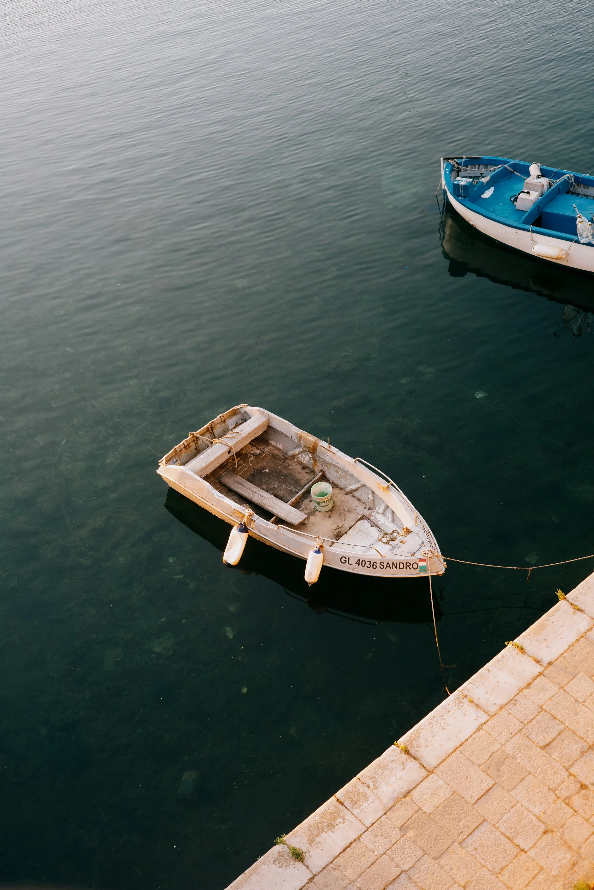 Two small boats are moored alongside a stone pier at the harbor, with calm water surrounding them in Italy.