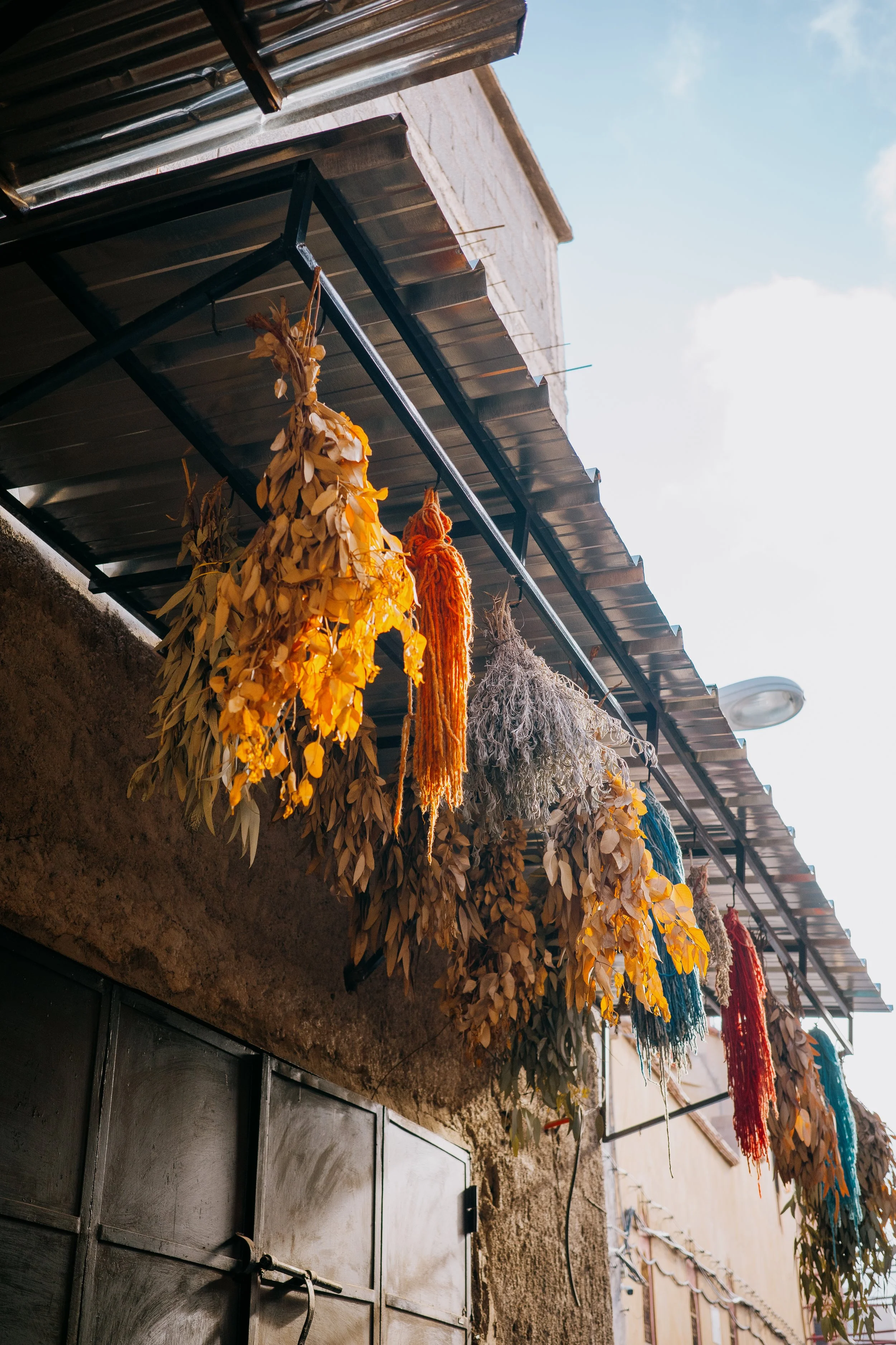 Colorful dried herbs and flowers hanging on a metal railing outside a building with a stone wall and a clear sky in Marrakech 