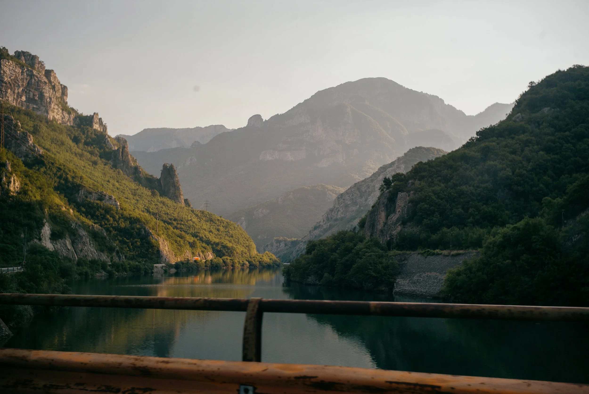 Mountains and a river with green trees along the banks, taken from a bridge or road.