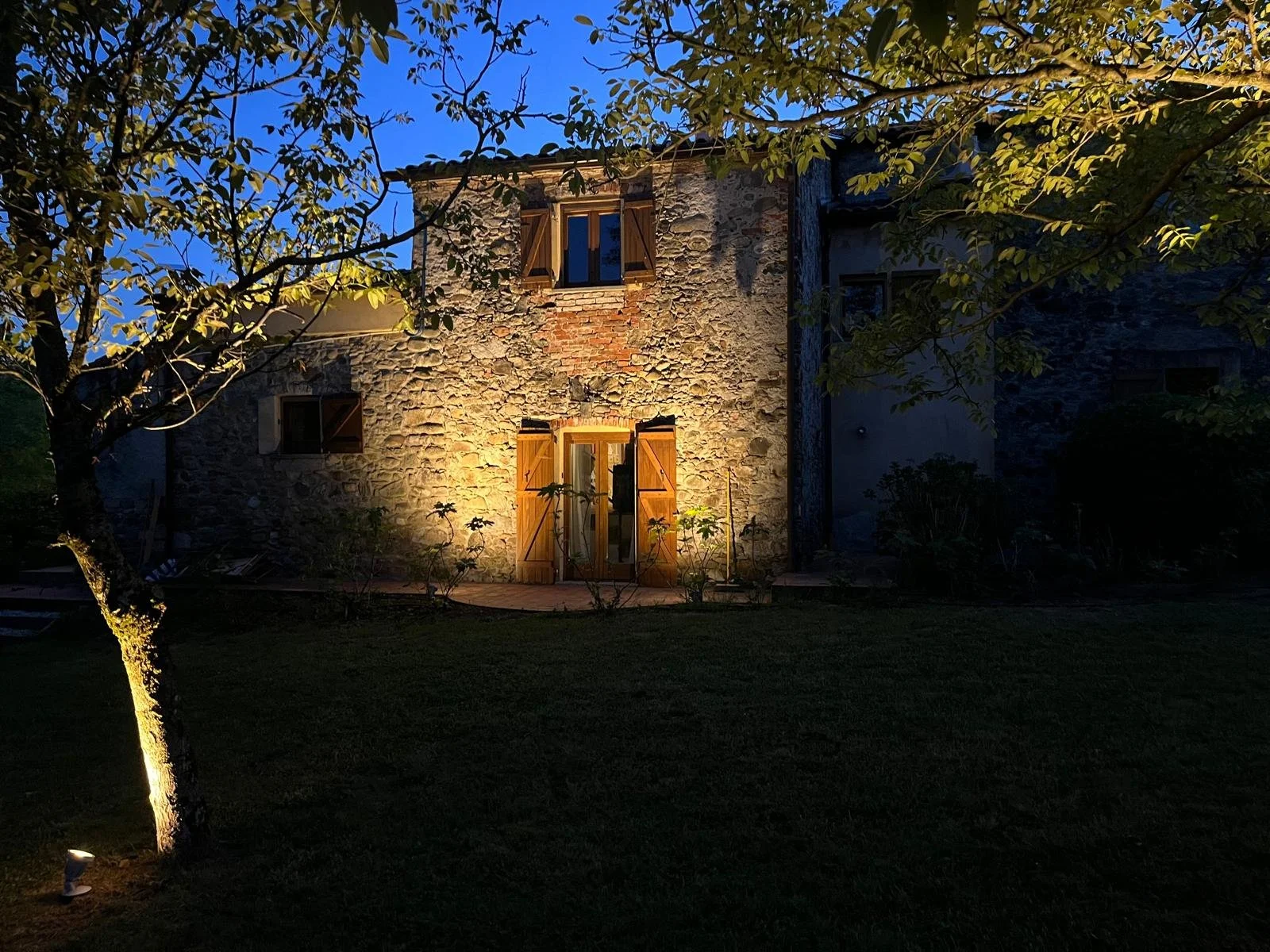 I Ginepri Country House in Northern Tuscany at dusk, with the stone house and garden softly illuminated