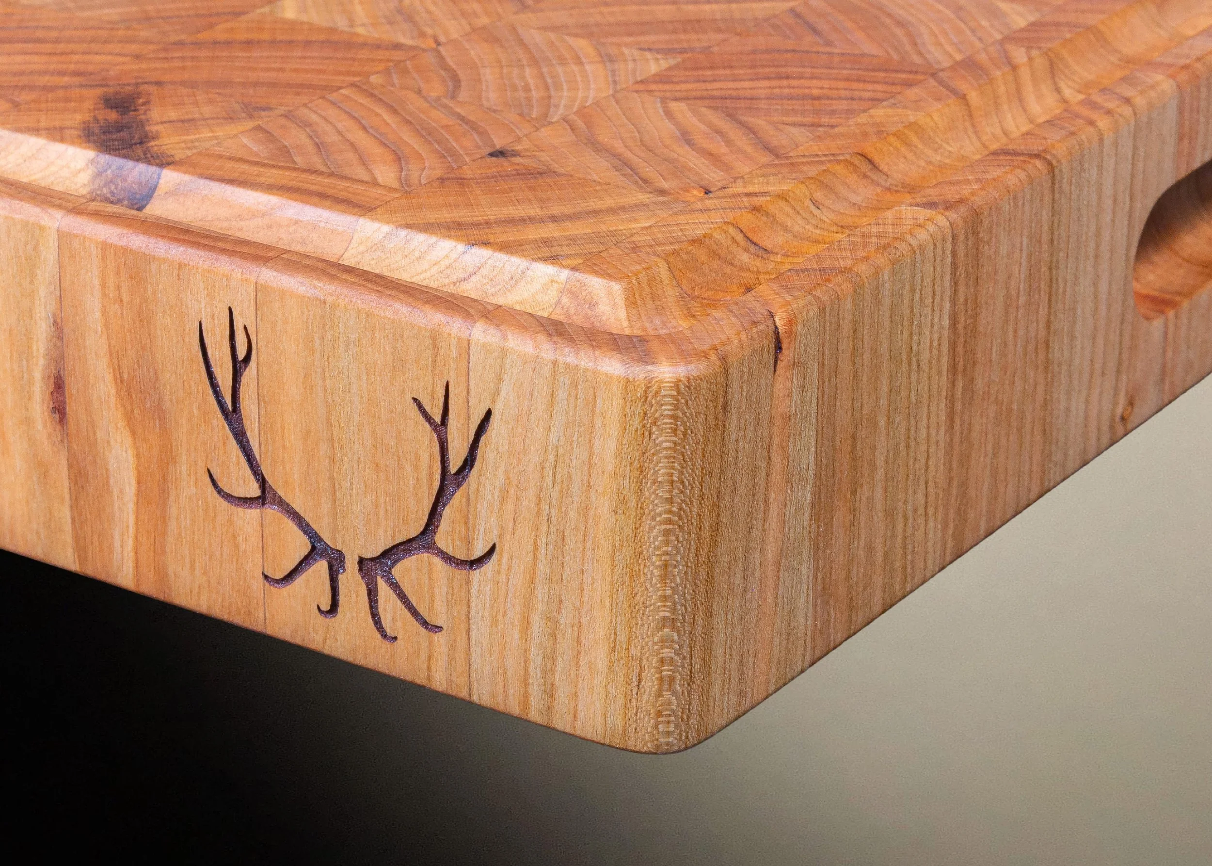 Close-up of a wooden cutting board with elk antlers laser etched on the side.