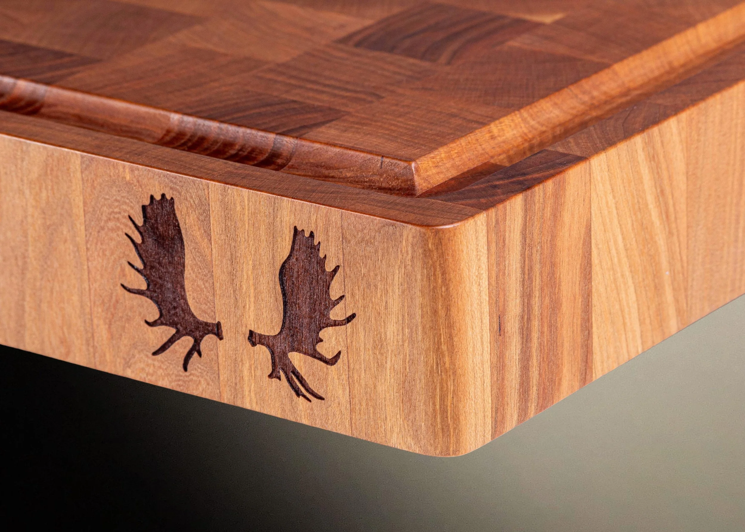 Close-up of a wooden cutting board with moose antlers laser etched on the side.