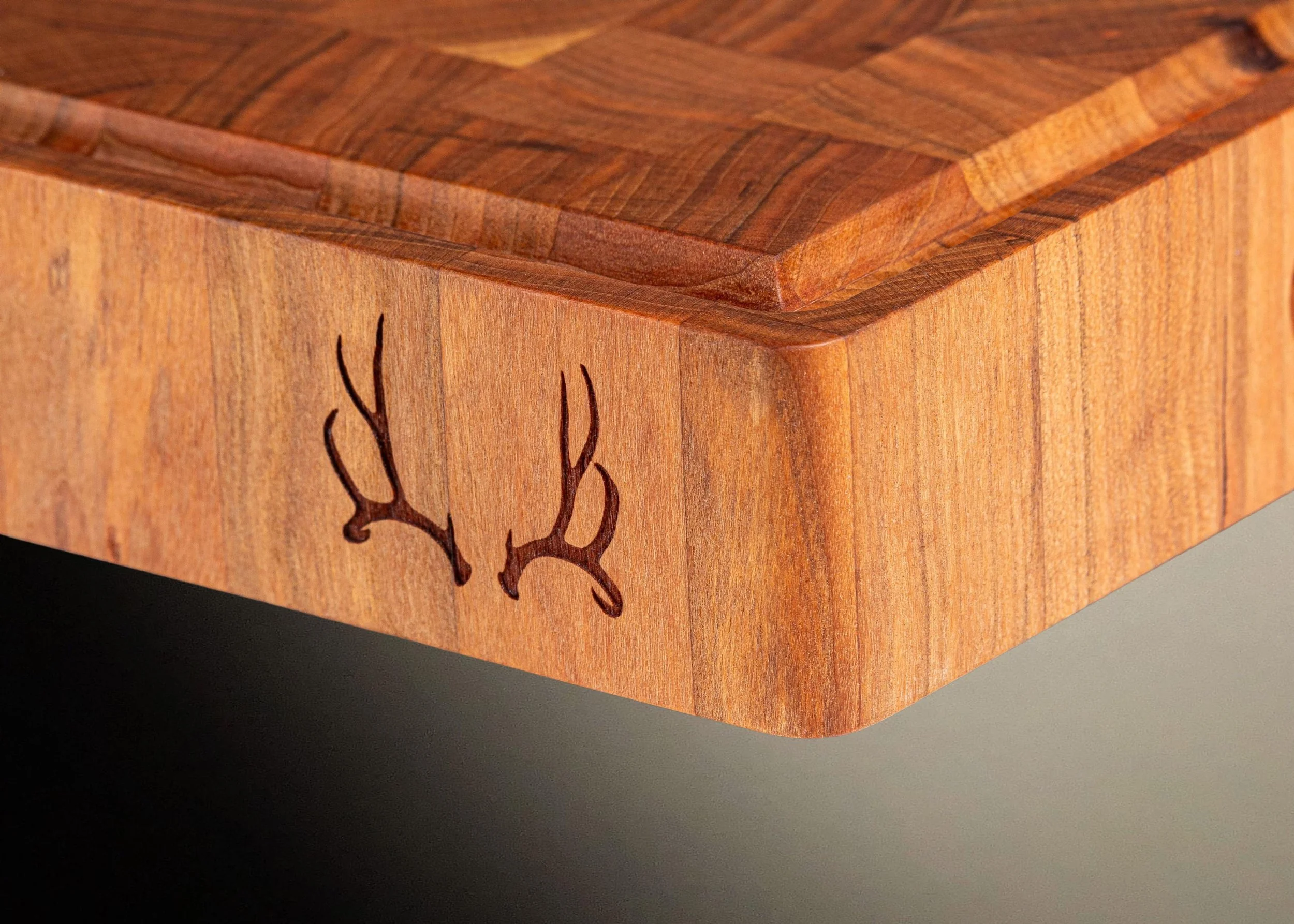 Close-up of a wooden cutting board with mule deer antlers laser etched on the side.
