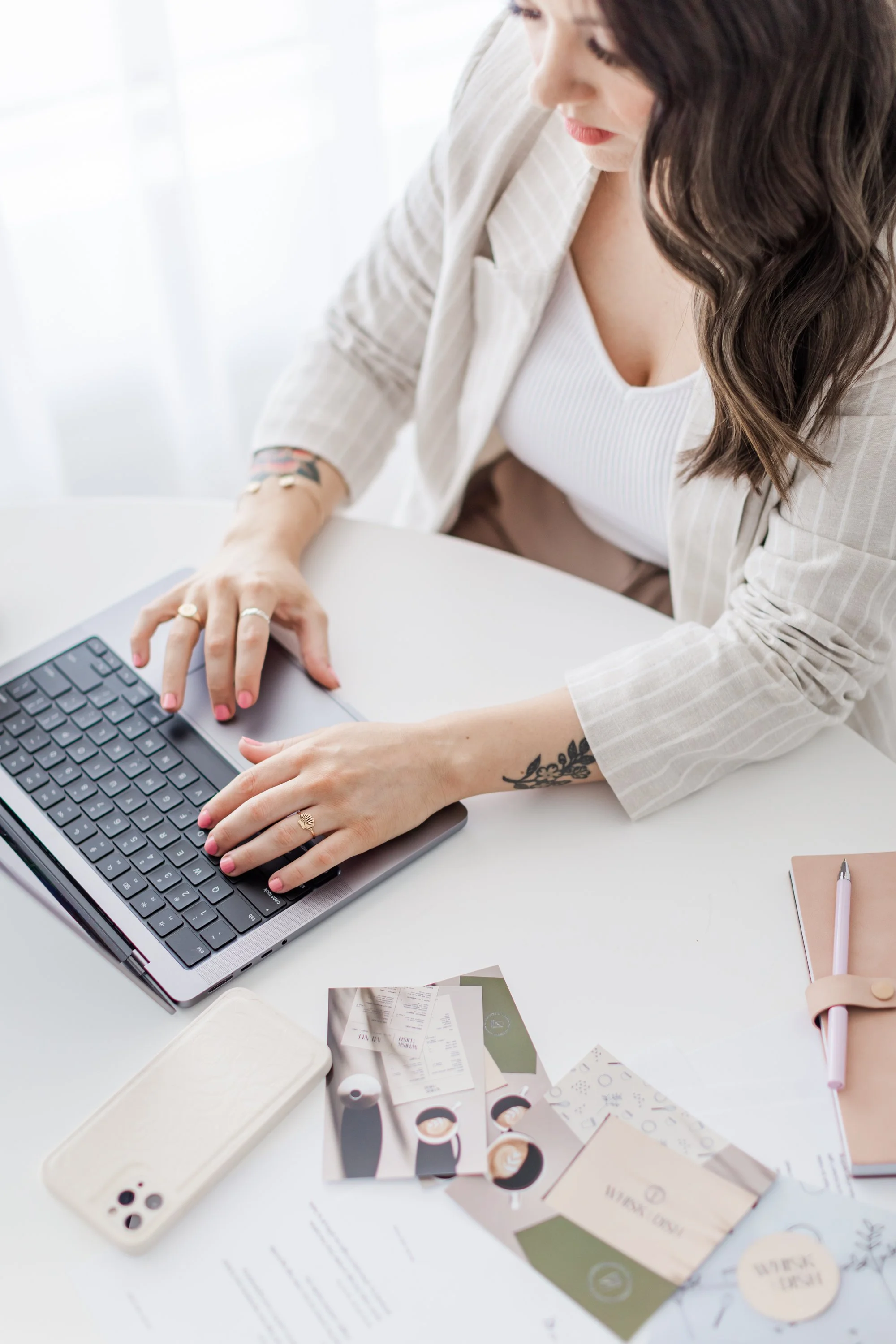 Woman typing on a laptop at a desk with a smartphone, business cards, and a notebook.