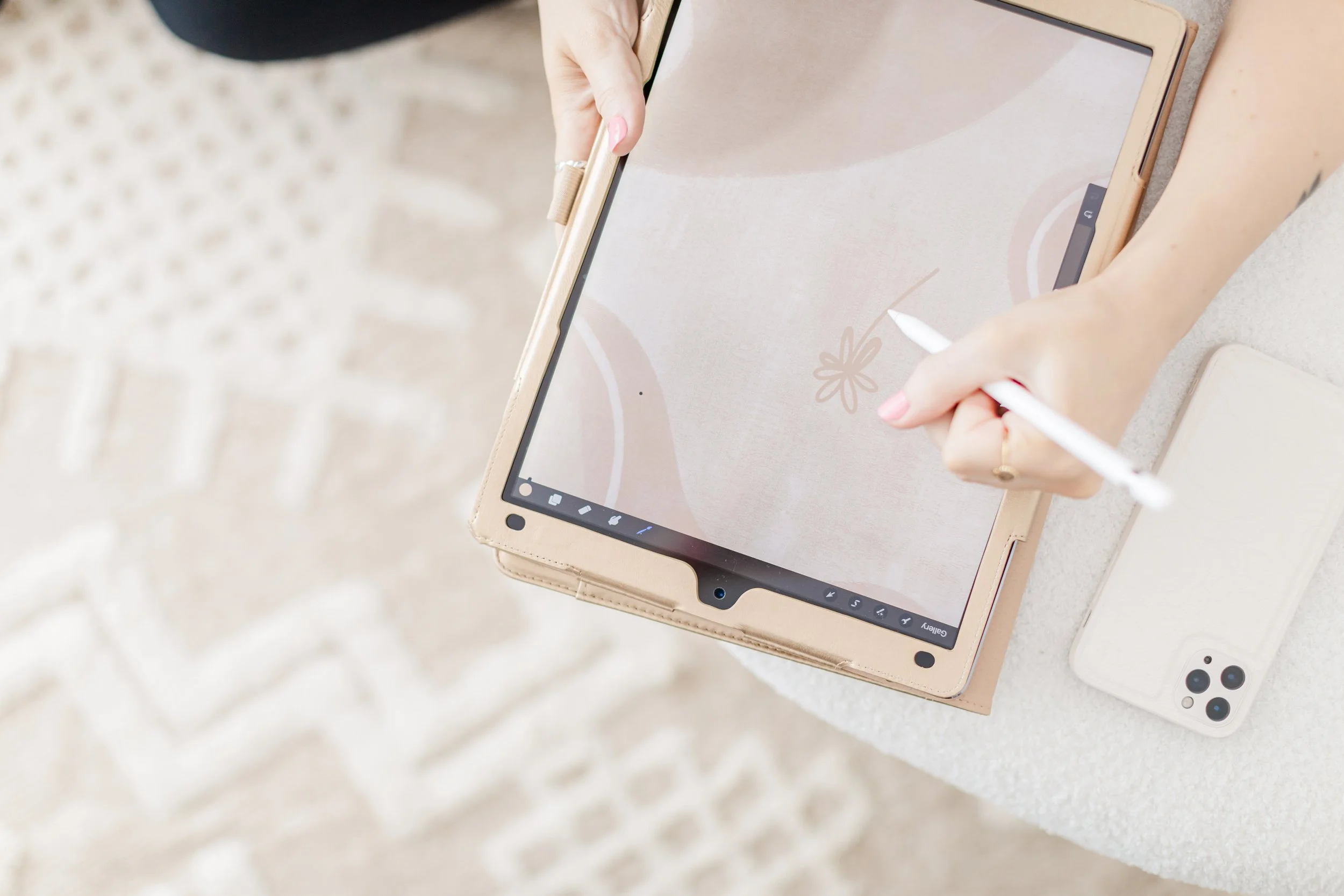 Person drawing on a tablet with a stylus, next to a smartphone on a textured surface.