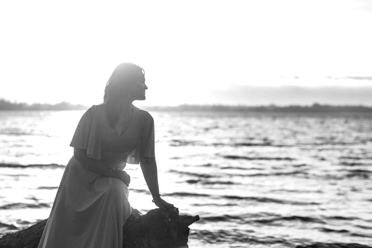 black and white photo of a girl sitting on a piece of driftwood in her senior prom dress