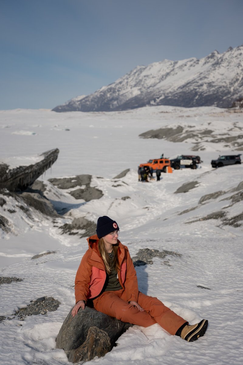Girl in orange snowsuit sitting near the knik glacier