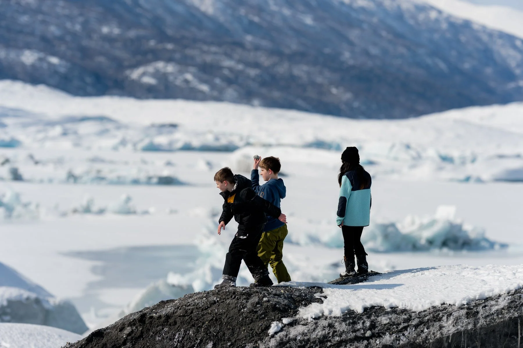 Photo of three kids playing on a glacier throwing rock.