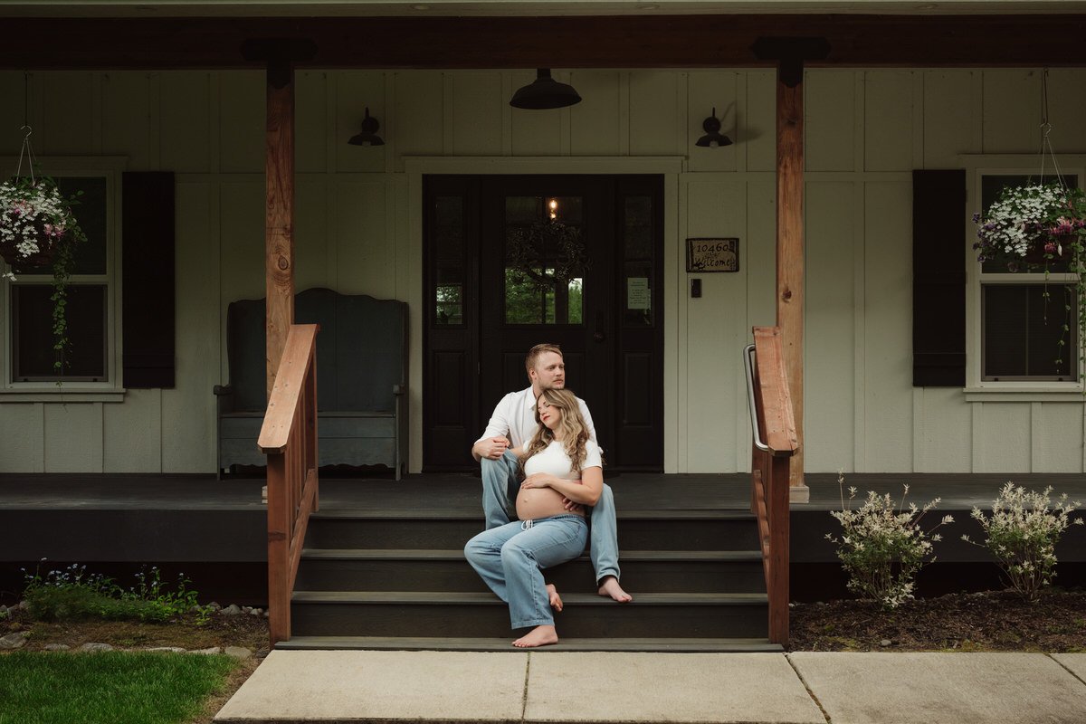 Pregnant couple sitting on the front stairs of a home in palmer alaska