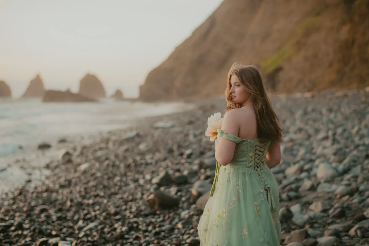 stunning portrait of high school senior girl in a green dress holding peonies along the oregon coast