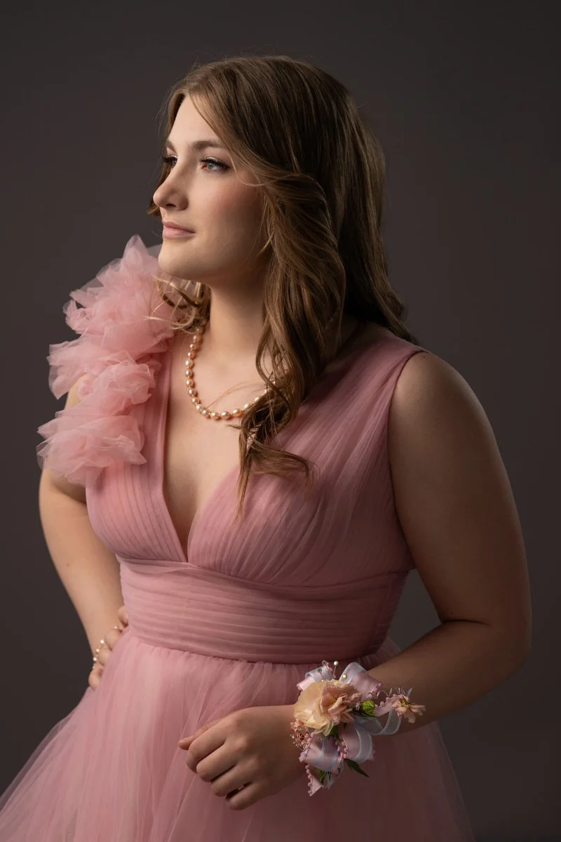 Portrait of a high school senior girl standing in a studio with her corsage in her prom gown for senior portraits
