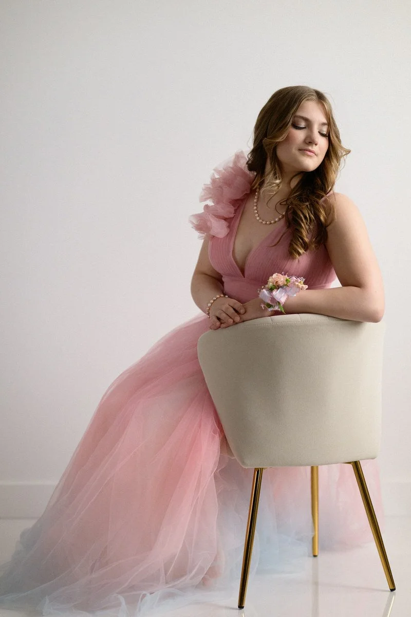 Girl in a gown poses for a portrait against a white wall in a studio in Palmer, Alaska