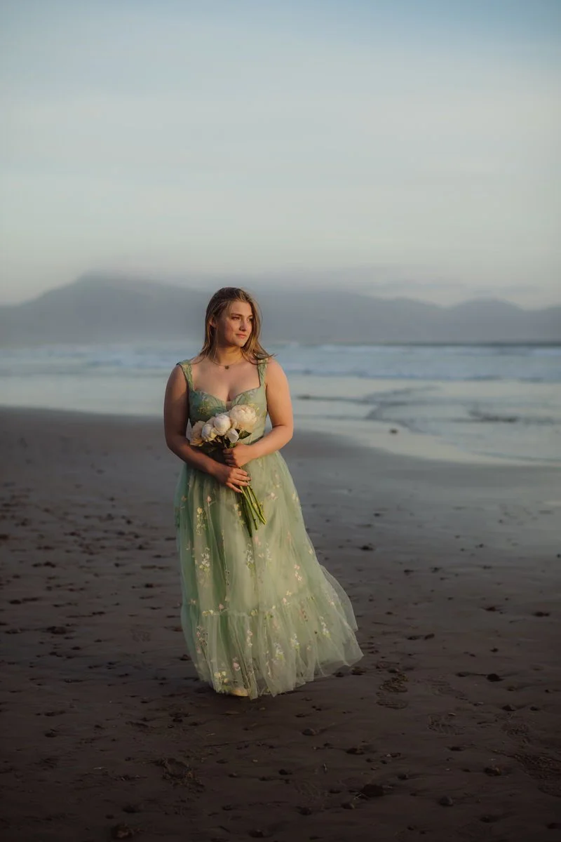 portrait of a girl walking along the ocean beach olding peonies wearing a green prom dress