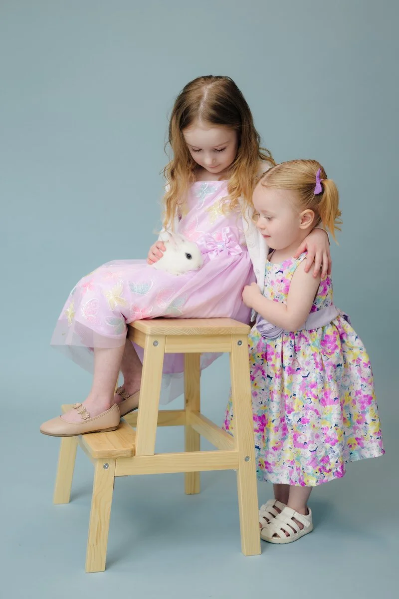 Girl and sister sitting on a chair holding a bunny with a blue background