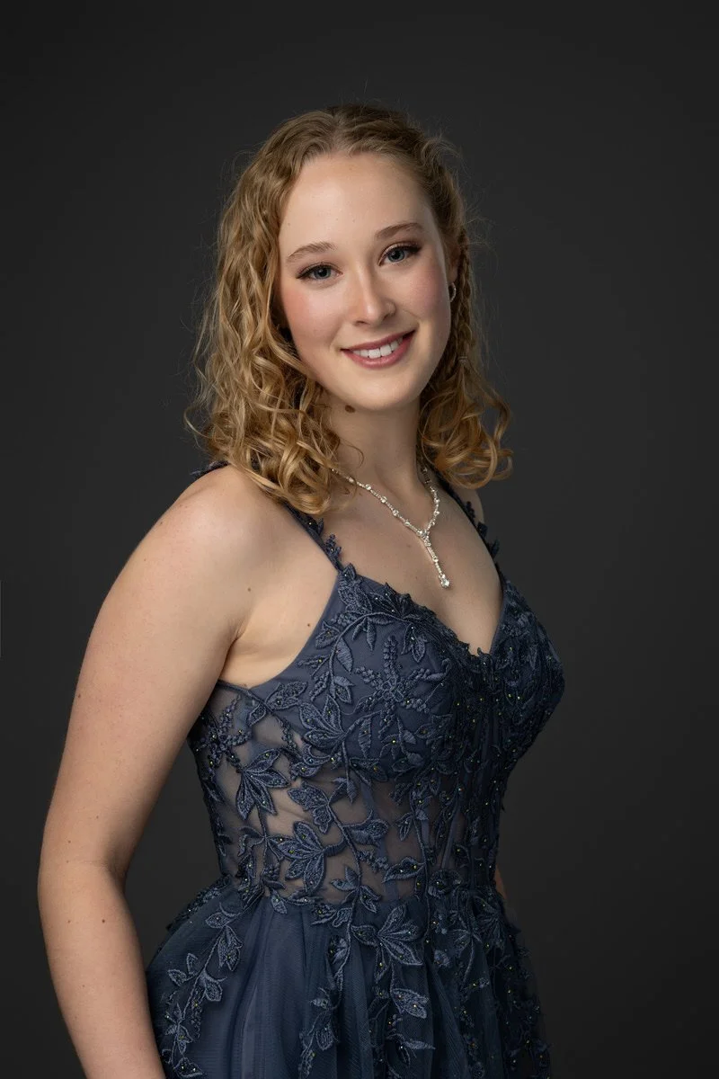 High school prom portrait taken in a studio against a gray background with a navy blue dress