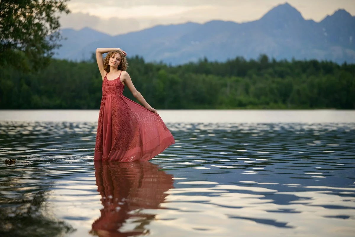 Portrait of a girl in a pink dress standing in a lake with the mountains behind her