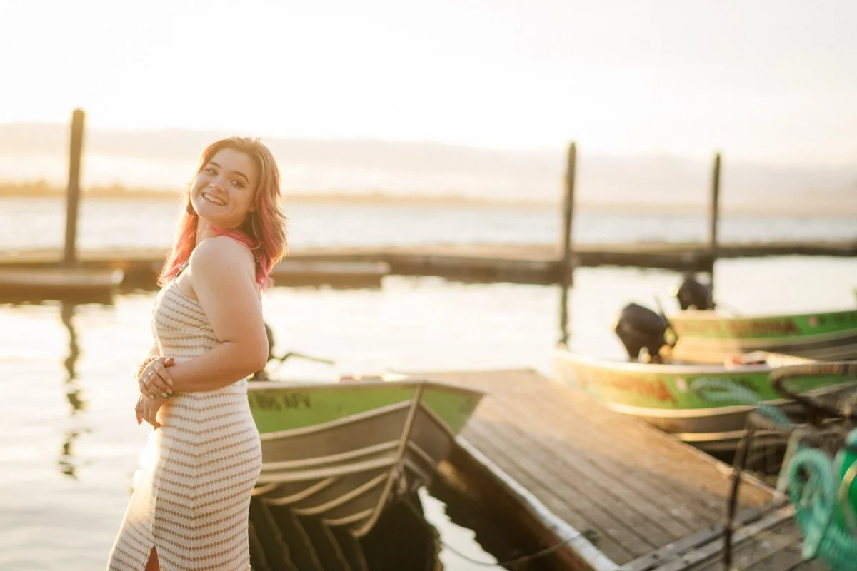 Portrait of a girl standing on Kelly's Brighton Marina in Oregon for senior portraits wearing a cream dress and boats behind her