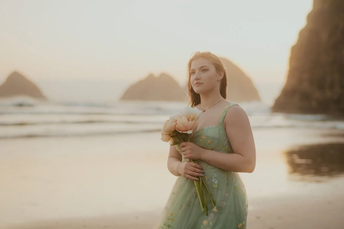 portrait of a teen walking along the beach in oregon holding flowers and wearing a green dress