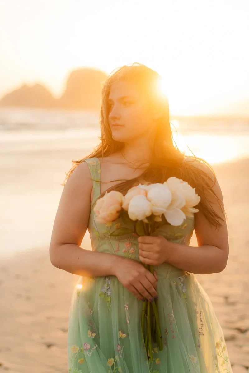 Beautiful backlit image of a high school girl holding peonies in her prom dress along the oregon coast