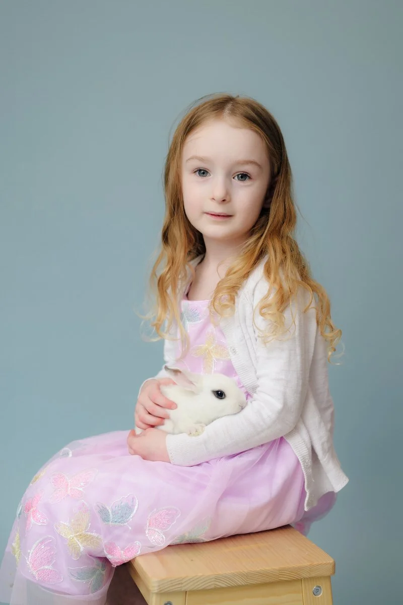 Little girl holds a blance de hotot rabbit with a blue background in her easter dress