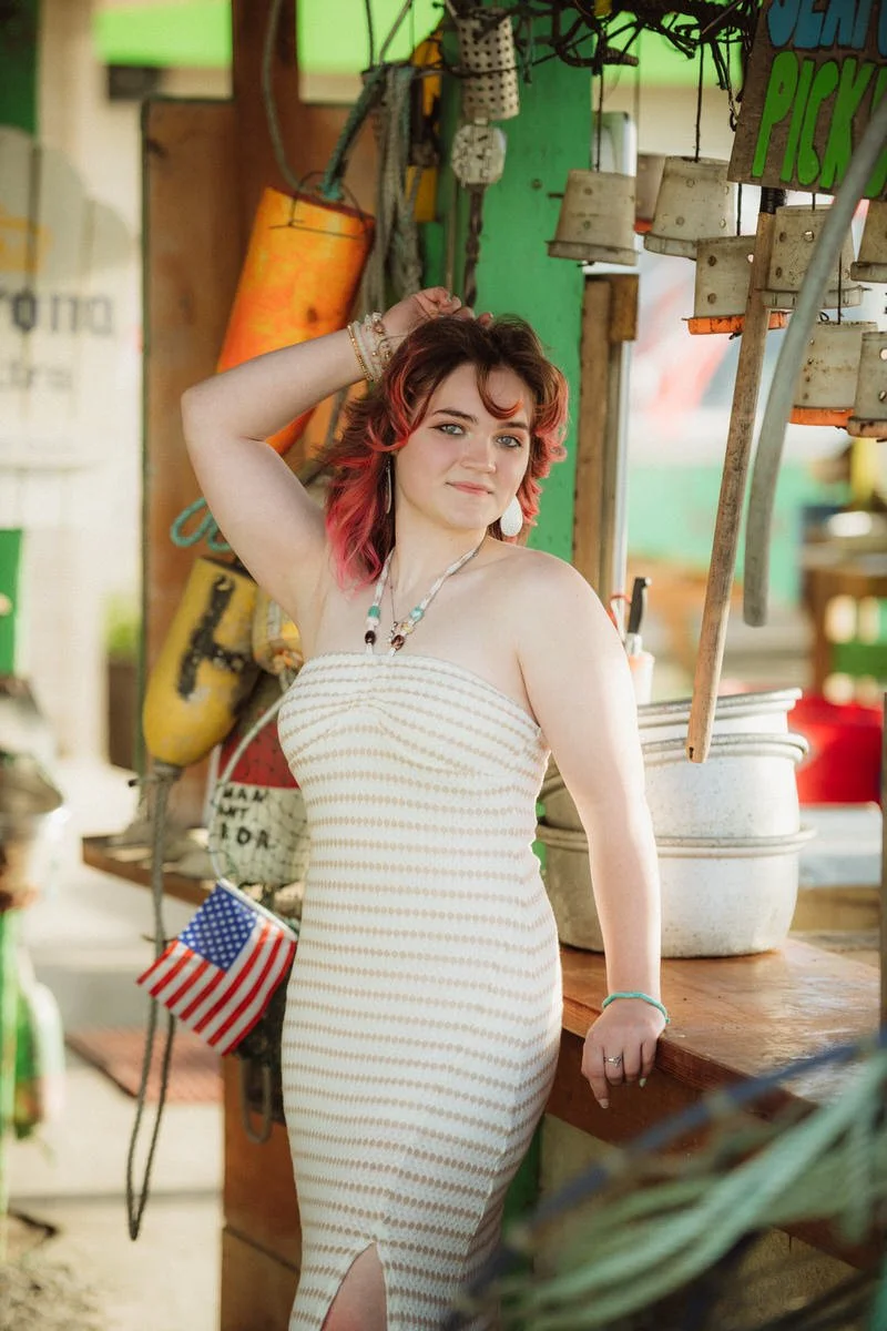 Portrait of a girl standing in a marina north of Rockaway. She has red hair and is wearing a brown and cream dress.