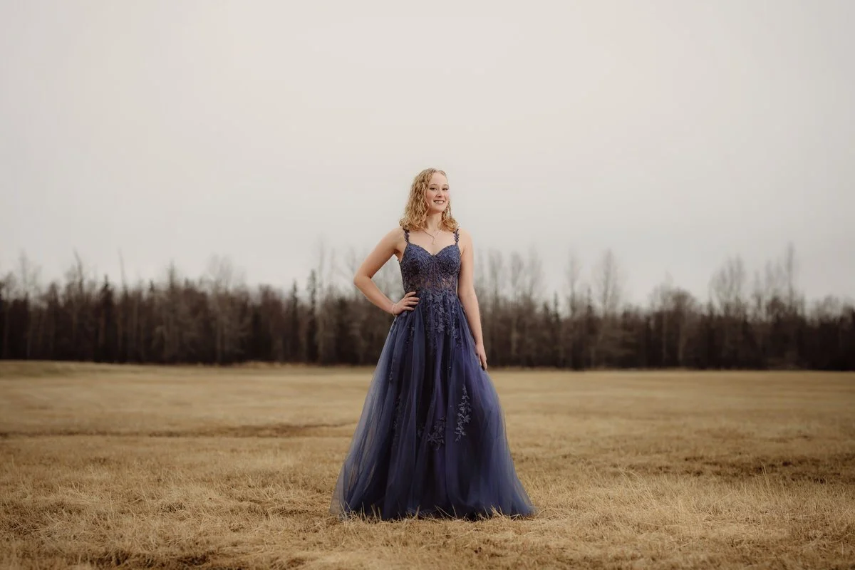 High school senior girl standing in a wheat field in her blue prom dress