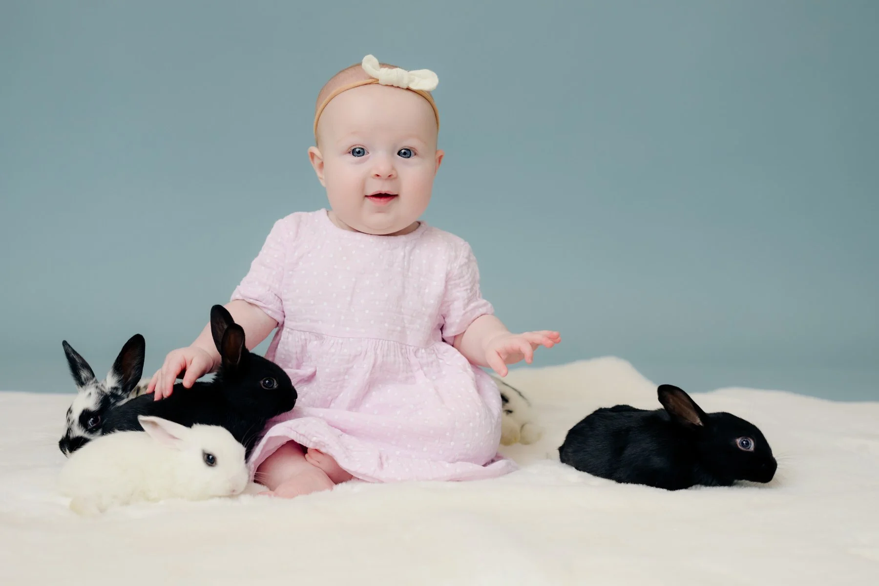 Little baby sitting with baby bunnies with a blue background.