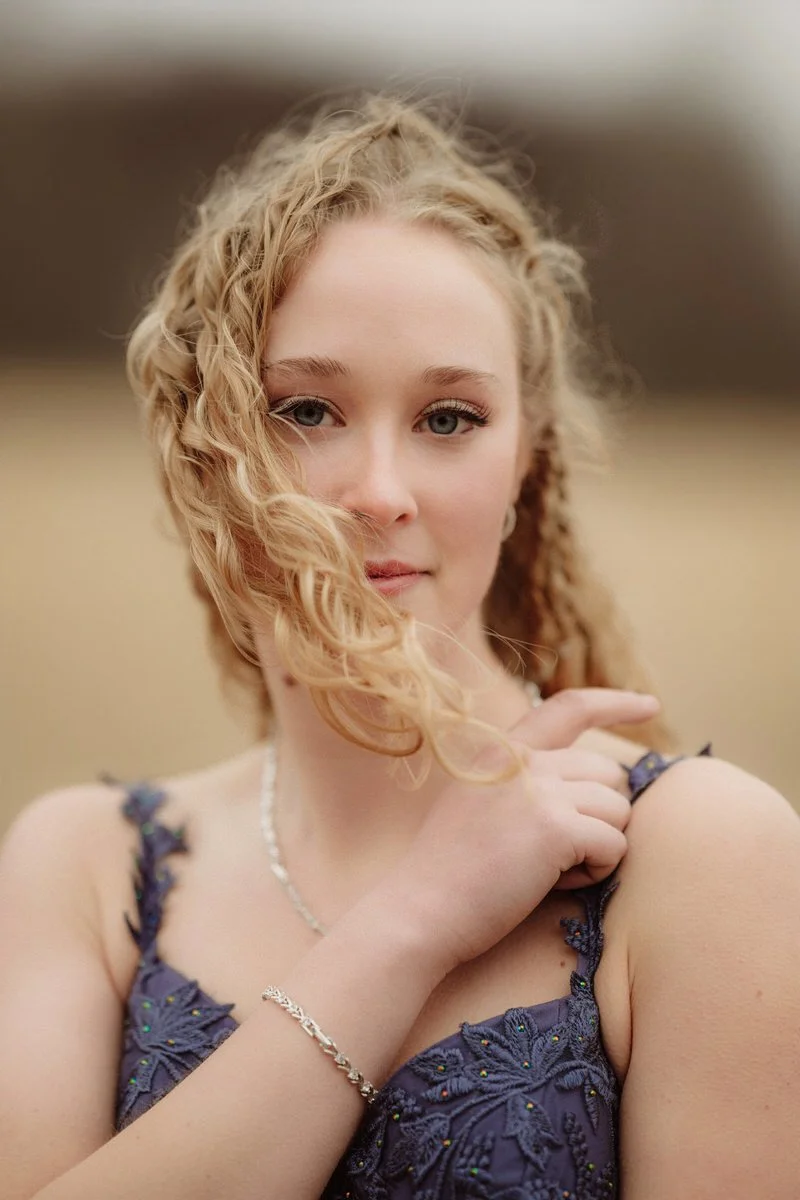 High School graduate staring into camera with her golden curly hair blowing in the wind