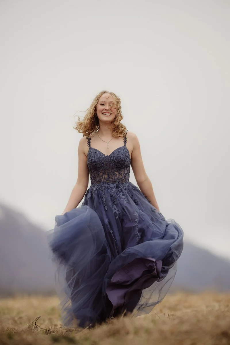Teenager running in a blue prom dress with her hair blowing wildly in the wind.