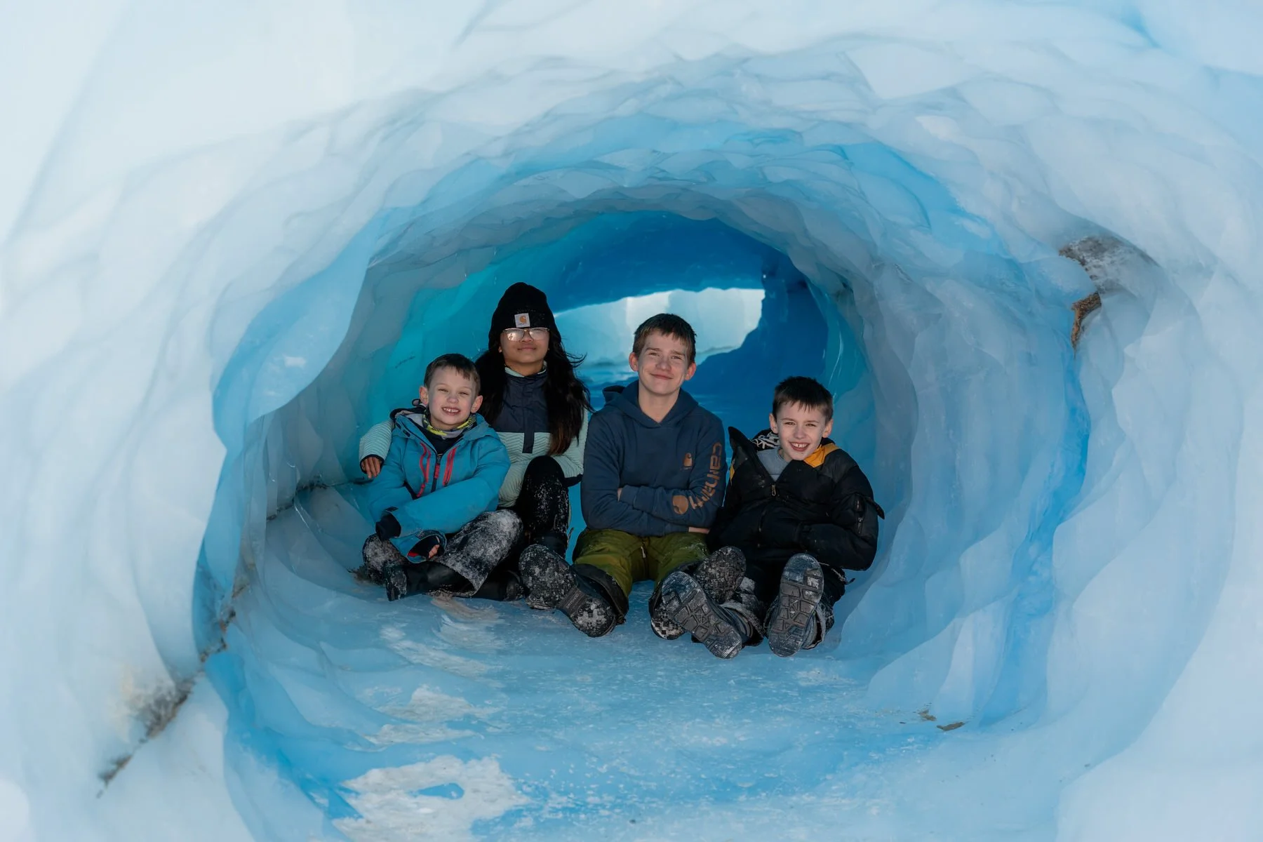 four kids sitting in an iceberg tunnel in Knik glacier