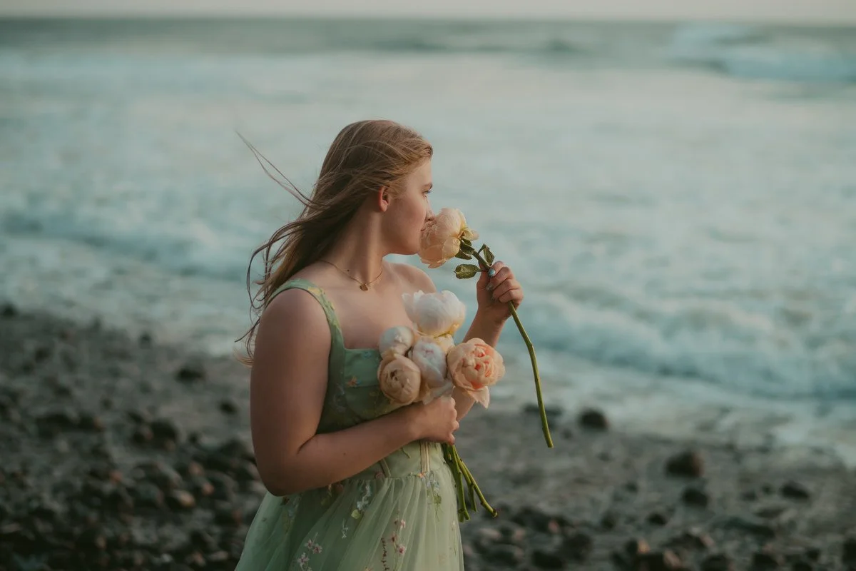 Portrait of high school senior smelling peonies while walking along the beach in oregon