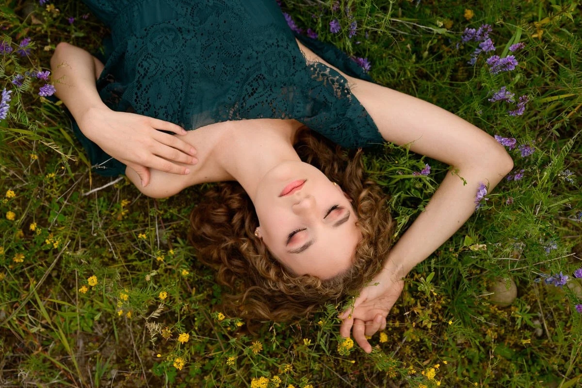 Portrait of a girl wearing a green dress laying in a field of wildflowers