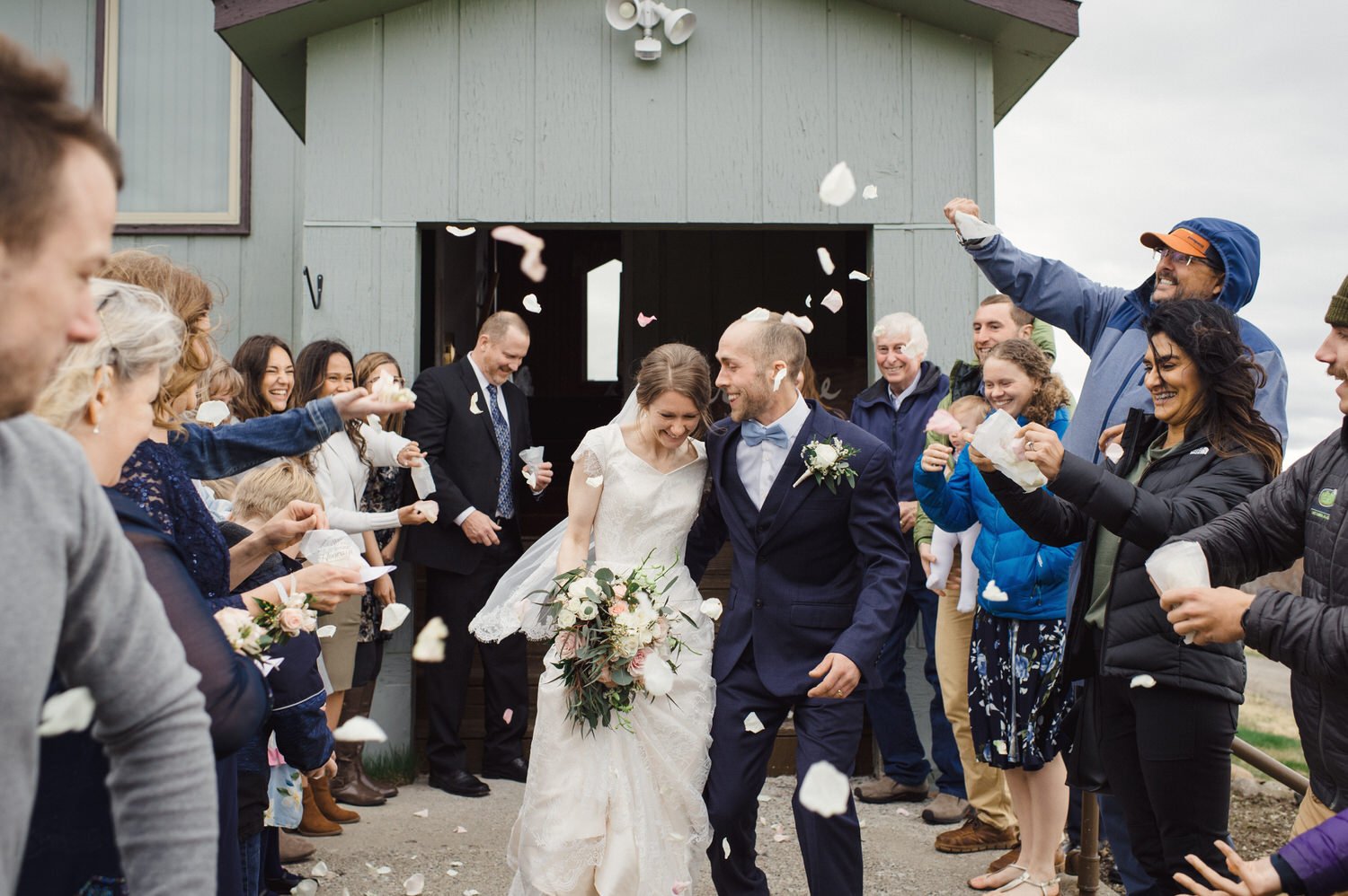 Bride and groom exiting a building, surrounded by guests throwing flower petals, celebrating a wedding.