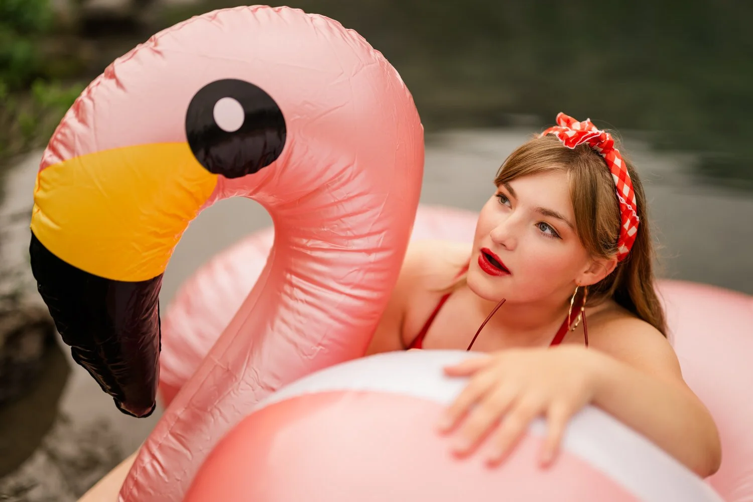 Vintage senior portrait shoot with a senior girl wearing a red hairband and sitting on a flamingo floaty