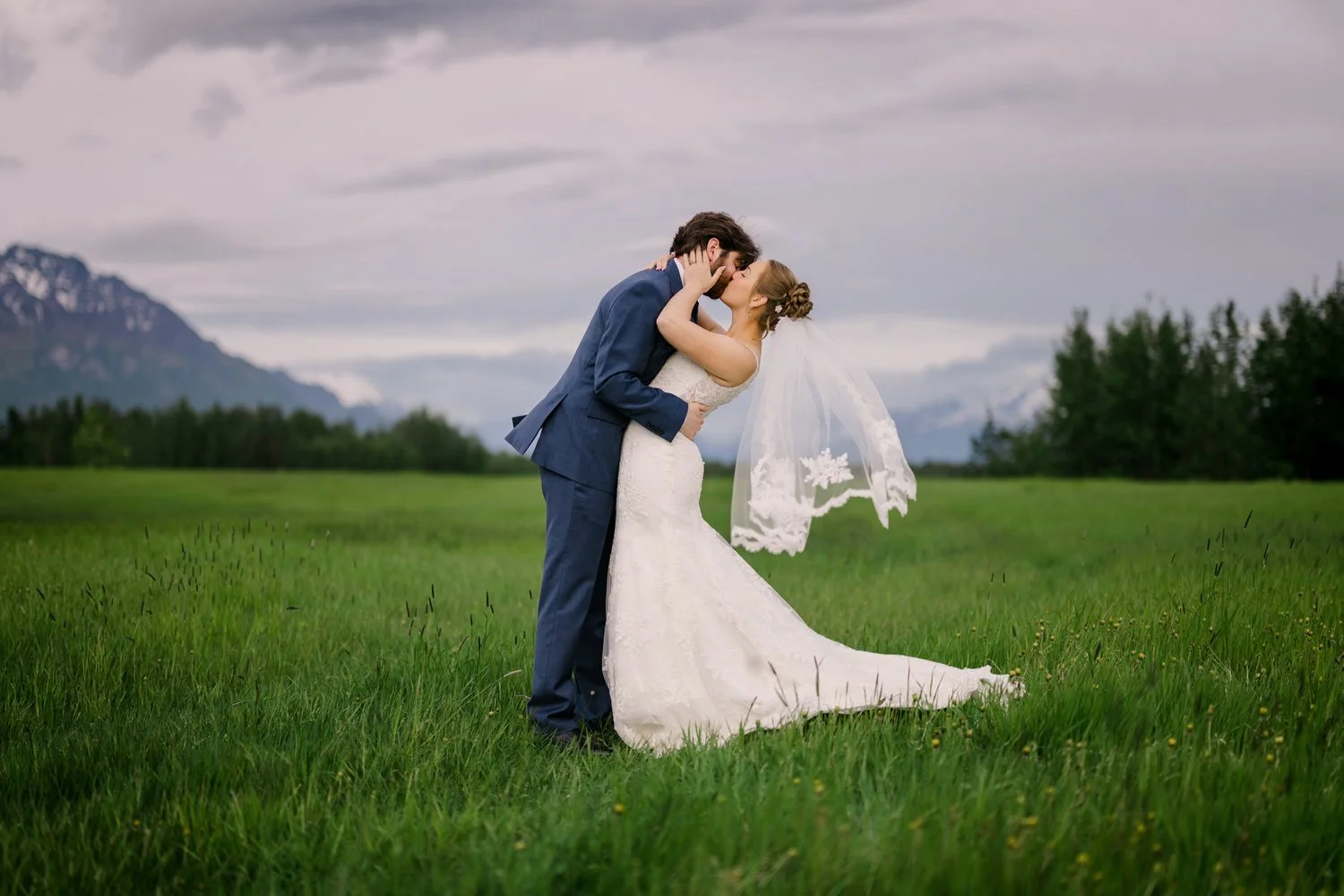 Portrait of a bride and groom kissing in a field of green with pioneer peak in the background.