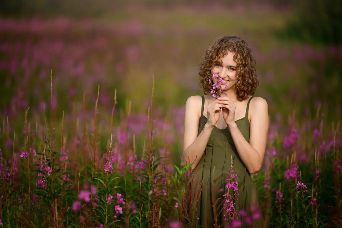 Portrait of a beautiful senior girl in a green dress standing in Pink fireweed field