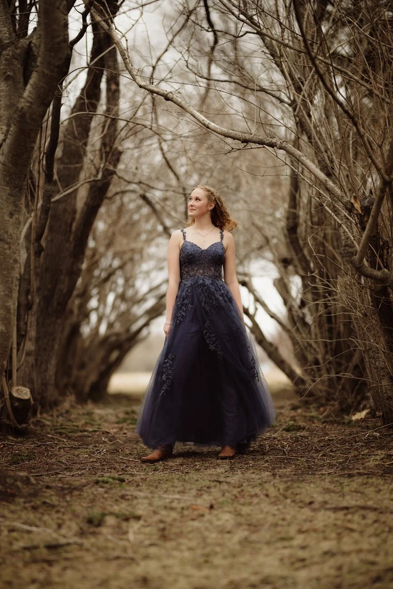 Girl standing in dead lilic bushes in her prom dress