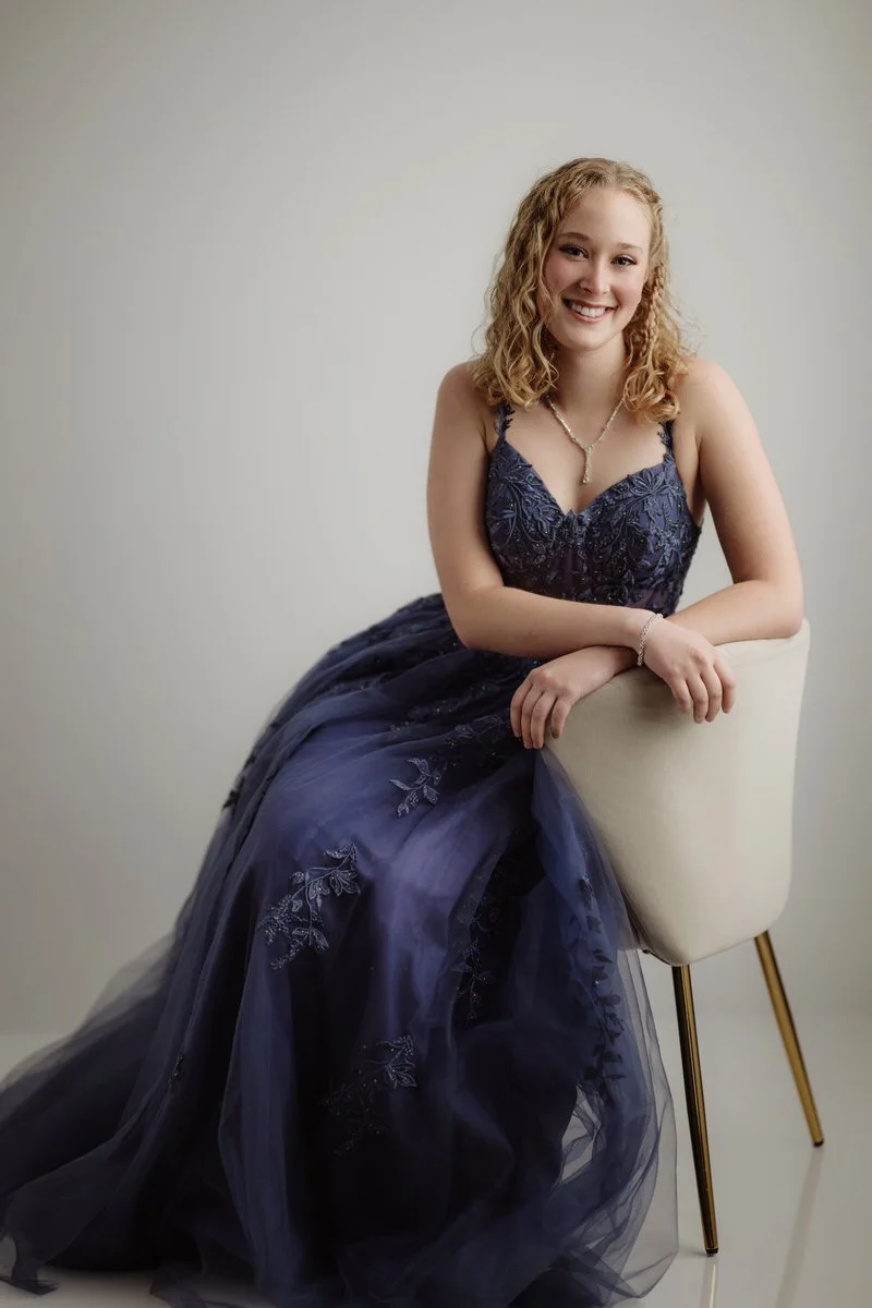 Studio senior prom portrait taken against a white wall and wearing a navy blue prom dress